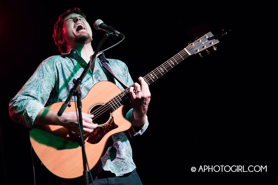 Brandon Bower singing and playing acoustic guitar on stage